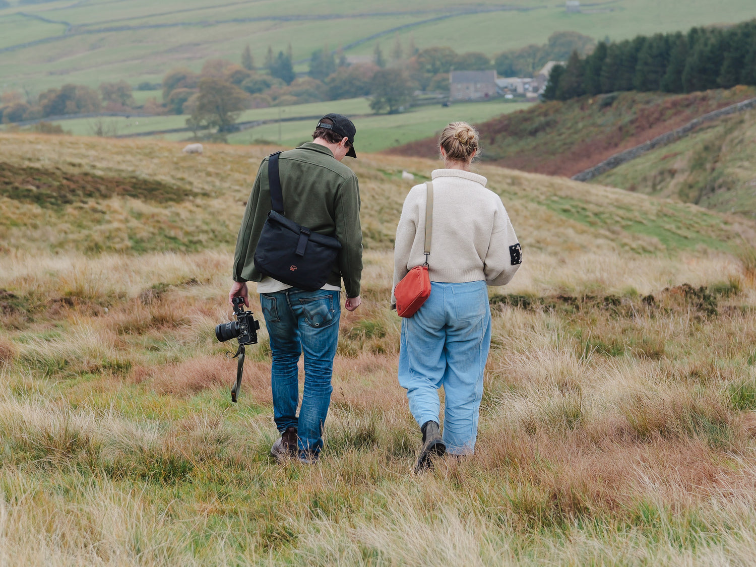 Two people walking through a scenic landscape with a camera and bags.