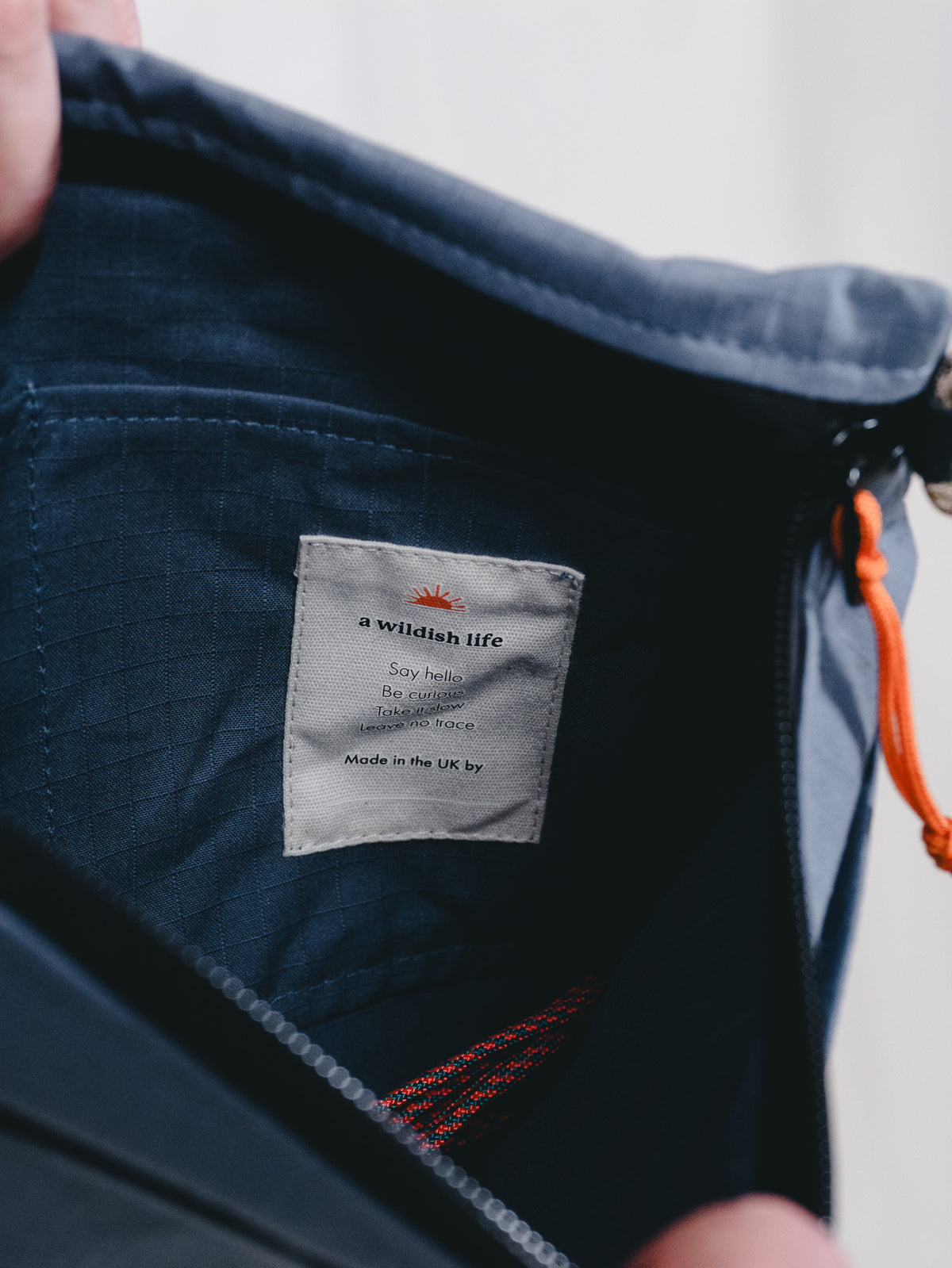 Close-up of the inside of a dark navy blue zippered pouch or bag, showing a sewn-in fabric label that reads 'a wildfish life' and 'Made in the UK by'.