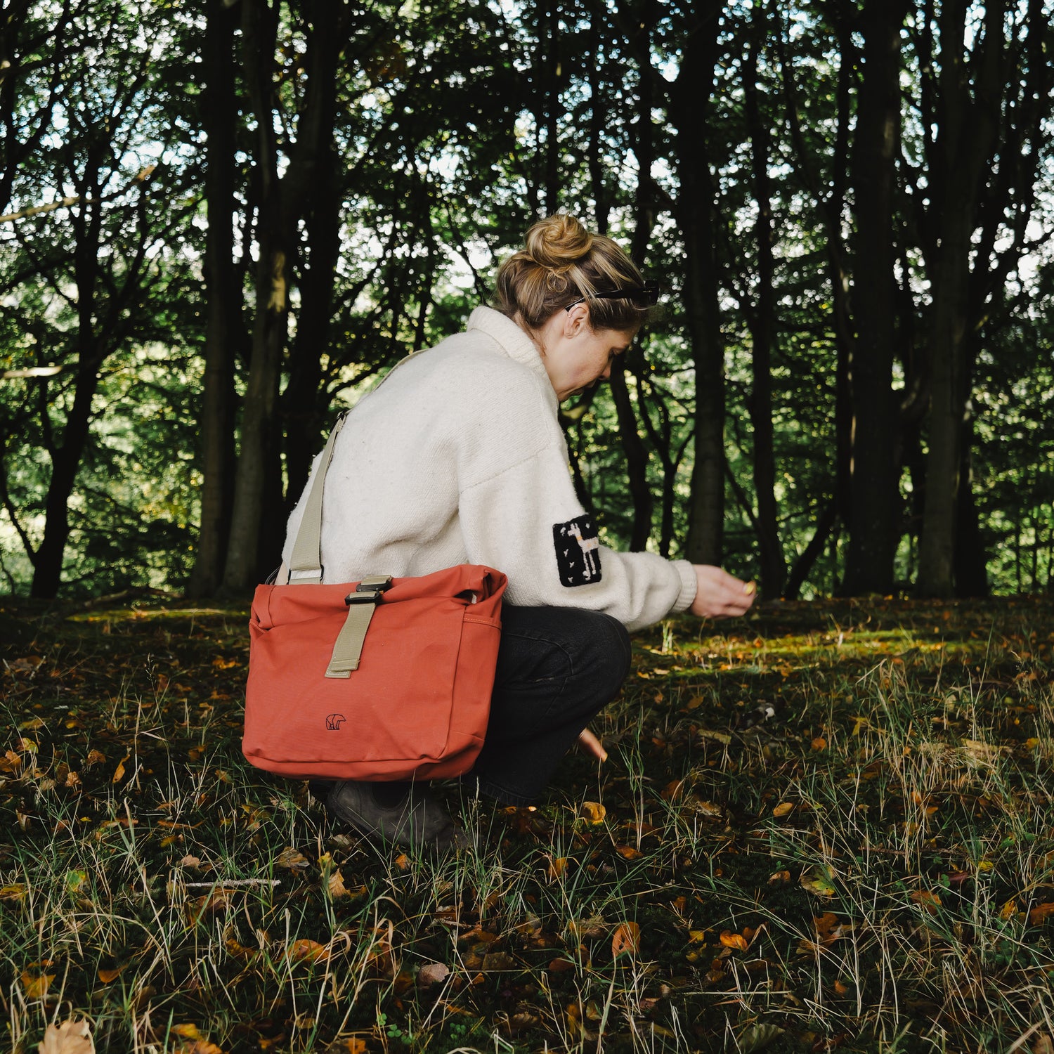 Person in a forest with a red bag, surrounded by trees and grass.